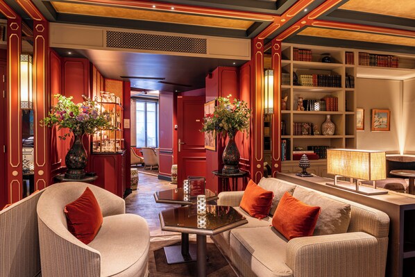 A well-lit, elegantly furnished lounge area with a sofa set, a coffee table, and a bookshelf filled with books and decorative items. - Hôtel de Montesquieu (Paris)
