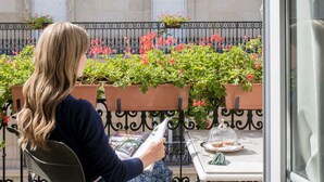 Eine Frau sitzt an einem Tisch auf einem Balkon mit Blumentöpfen und Blumen.