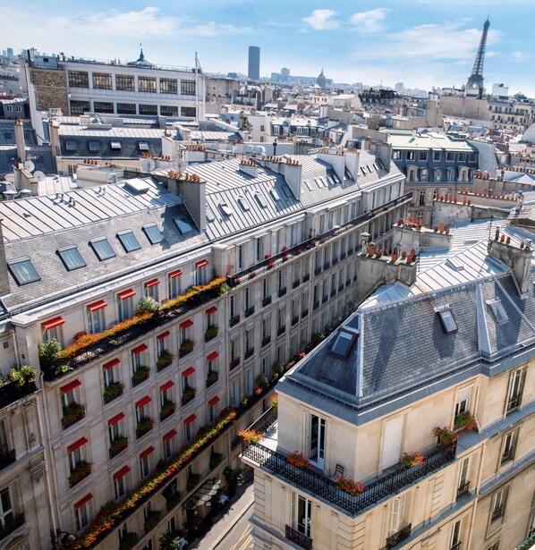 A multi-story building with a row of balconies, each with red awnings and potted plants. - Hôtel de Montesquieu (Paris)