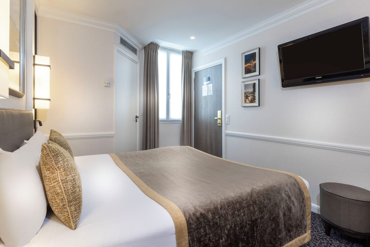 A hotel room with a bed, a television, and a door.