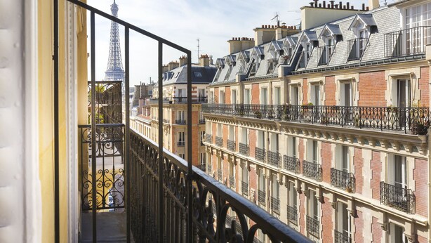 A balcony with wrought iron railings overlooking a row of Parisian buildings, including a view of the Eiffel Tower in the distance. - Elysees Union Hotel (Paris)