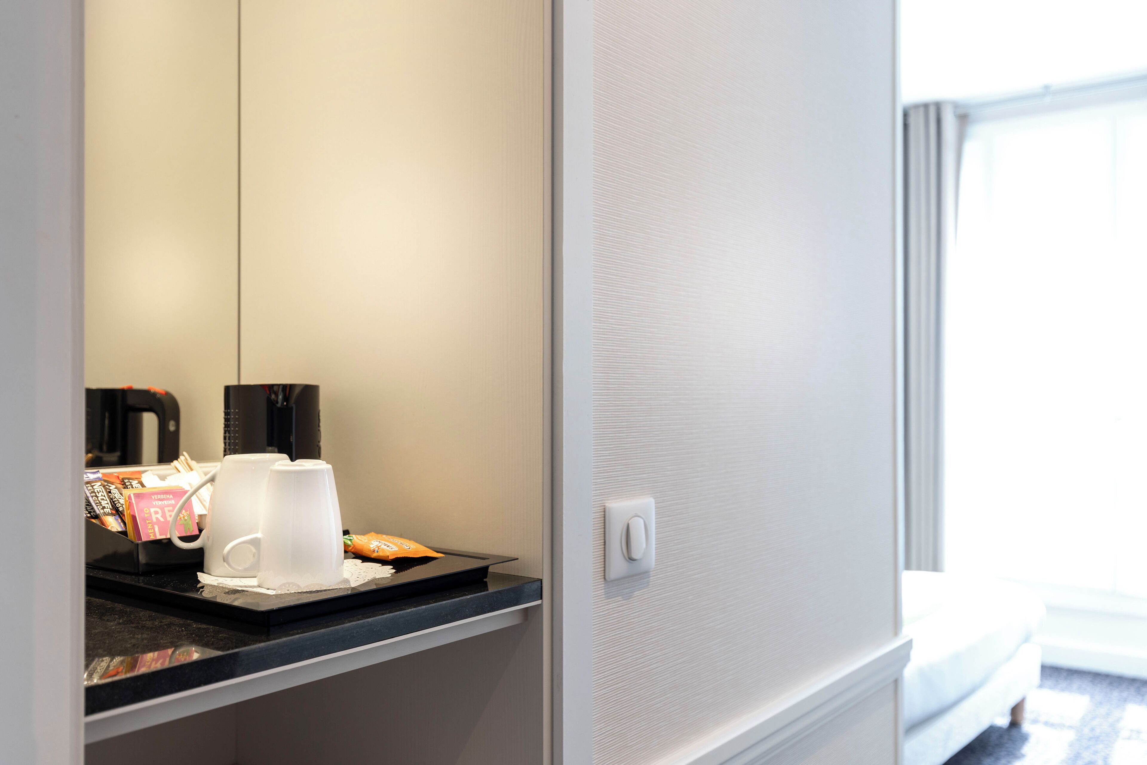 Quarto de hotel com espaço para café, cama e janela.