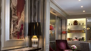 A well-lit lobby with a red carpet, a seating area with a red armchair, a table with a lamp, and a bookshelf with decorative items. - Elysees Union Hotel (Paris)
