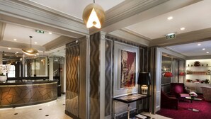 A modern lobby with a reception desk, a marble wall with a geometric pattern, a glass display case, and a red carpeted area. - Elysees Union Hotel (Paris)