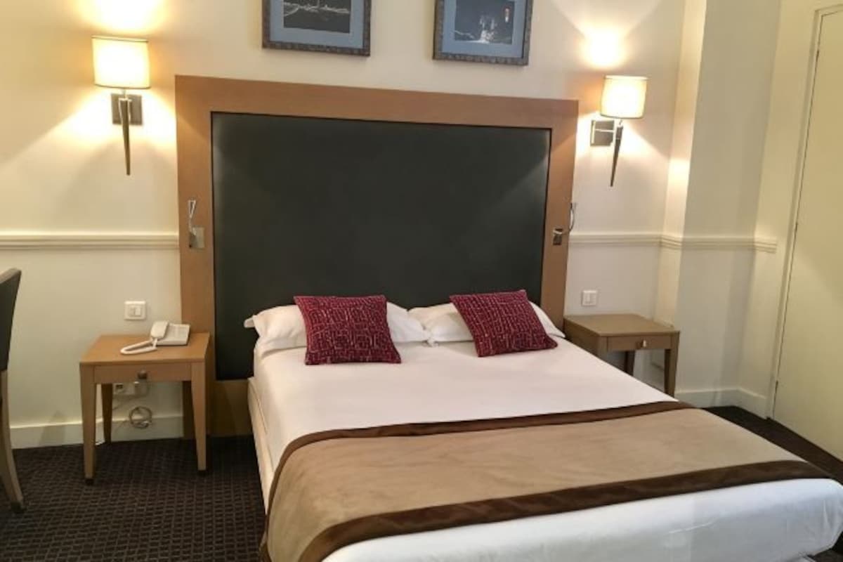 A hotel room with a large bed, two bedside tables, a chair, and a desk with a phone.