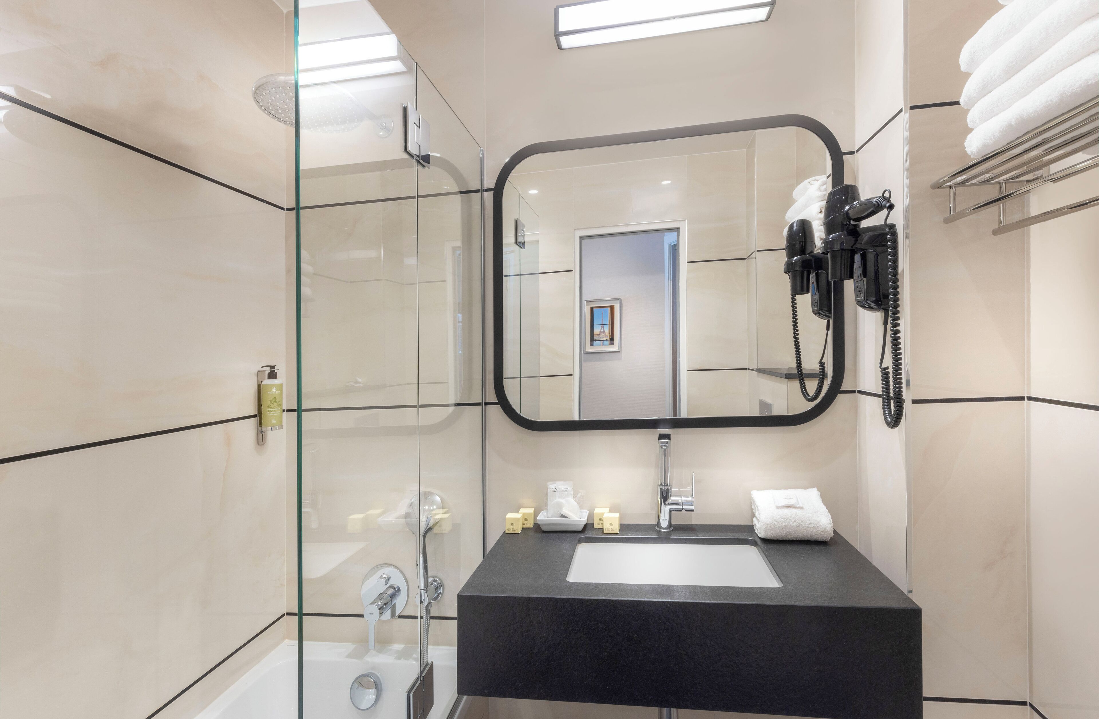 A modern bathroom with a glass shower enclosure, a black sink, and a hairdryer mounted on the wall.