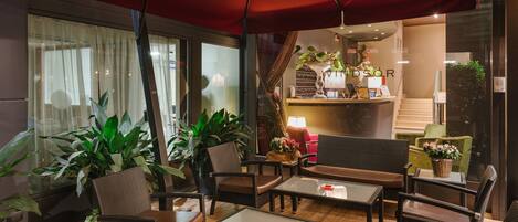 Un rincón exterior acogedor con mobiliario de mimbre y un paraguas rojo, con vista a un bar y una escalera.