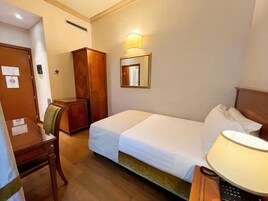 Een hotelkamer met een bed, een bureau, een stoel, een kledingkast, een spiegel en een lamp.