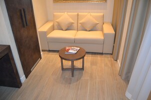 A modern living room with a beige sofa, two decorative pillows, a round wooden coffee table with a magazine, and a wooden floor.