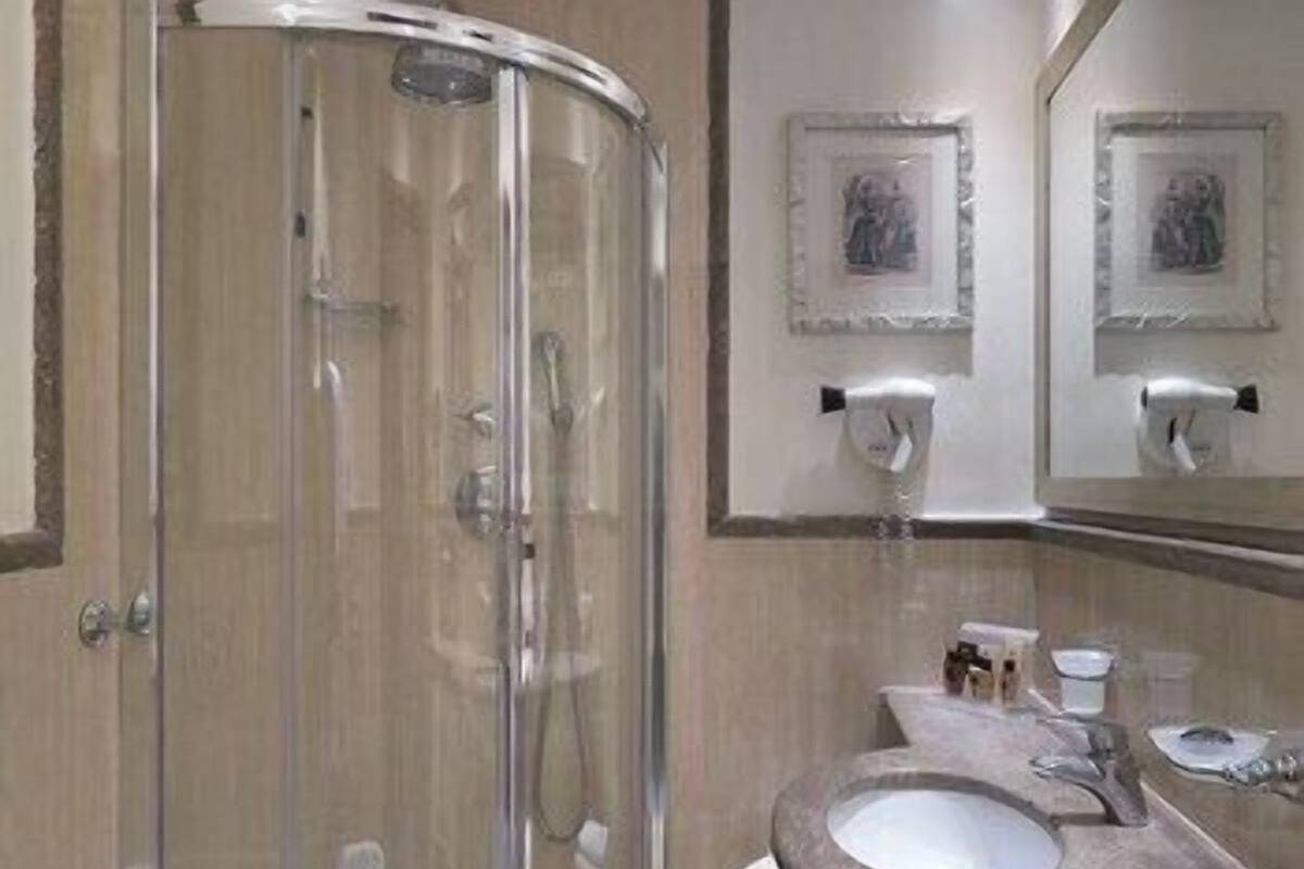 A bathroom with a glass shower enclosure, a sink, and a mirror.