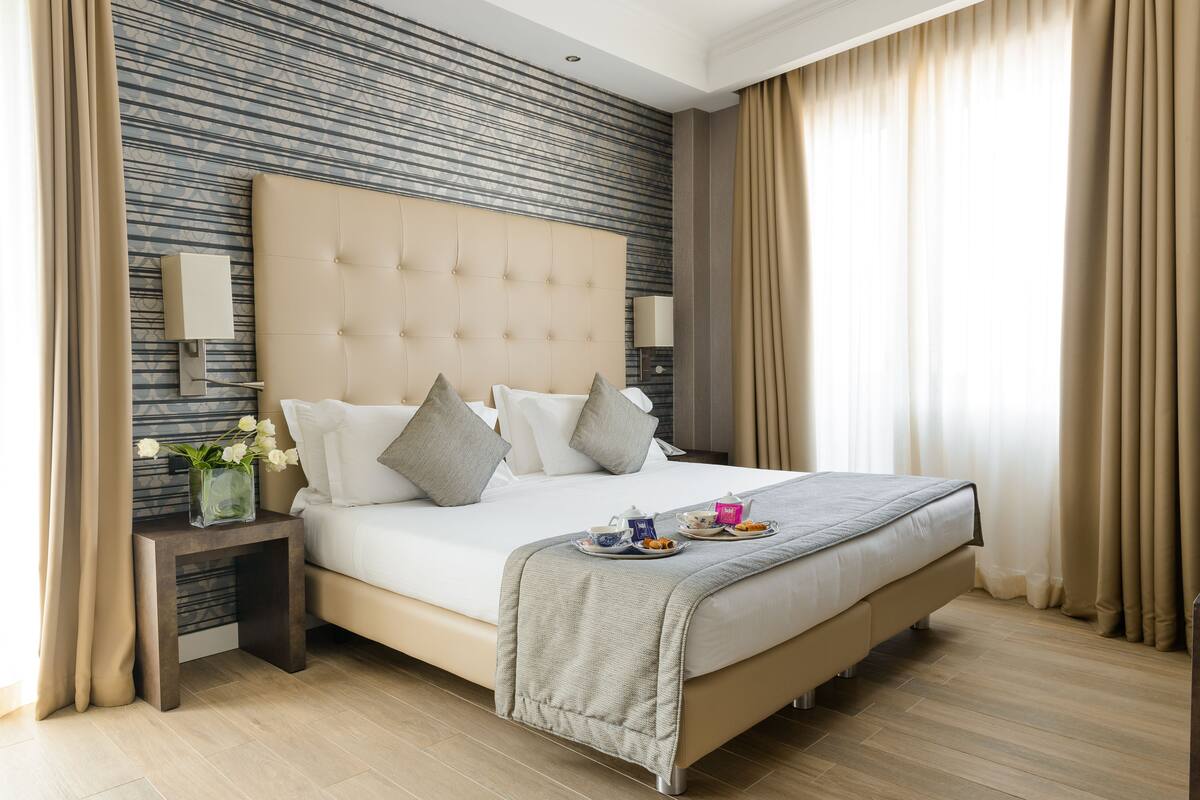 A spacious bedroom with a large bed, a nightstand with a lamp, and a vase of flowers.