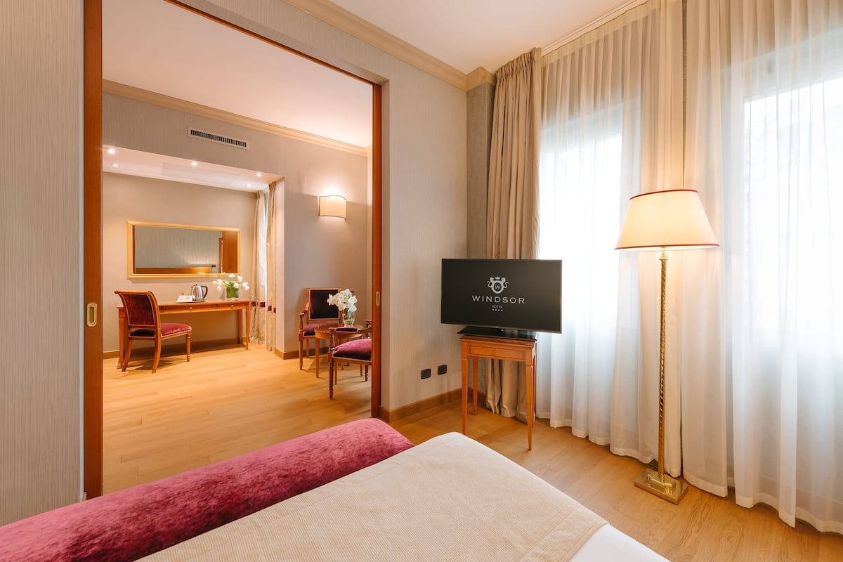 A hotel room with a bed, a desk with a chair, a television, and a lamp.