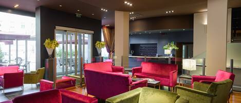 A lobby with red and green chairs, a reception desk, and a large window.