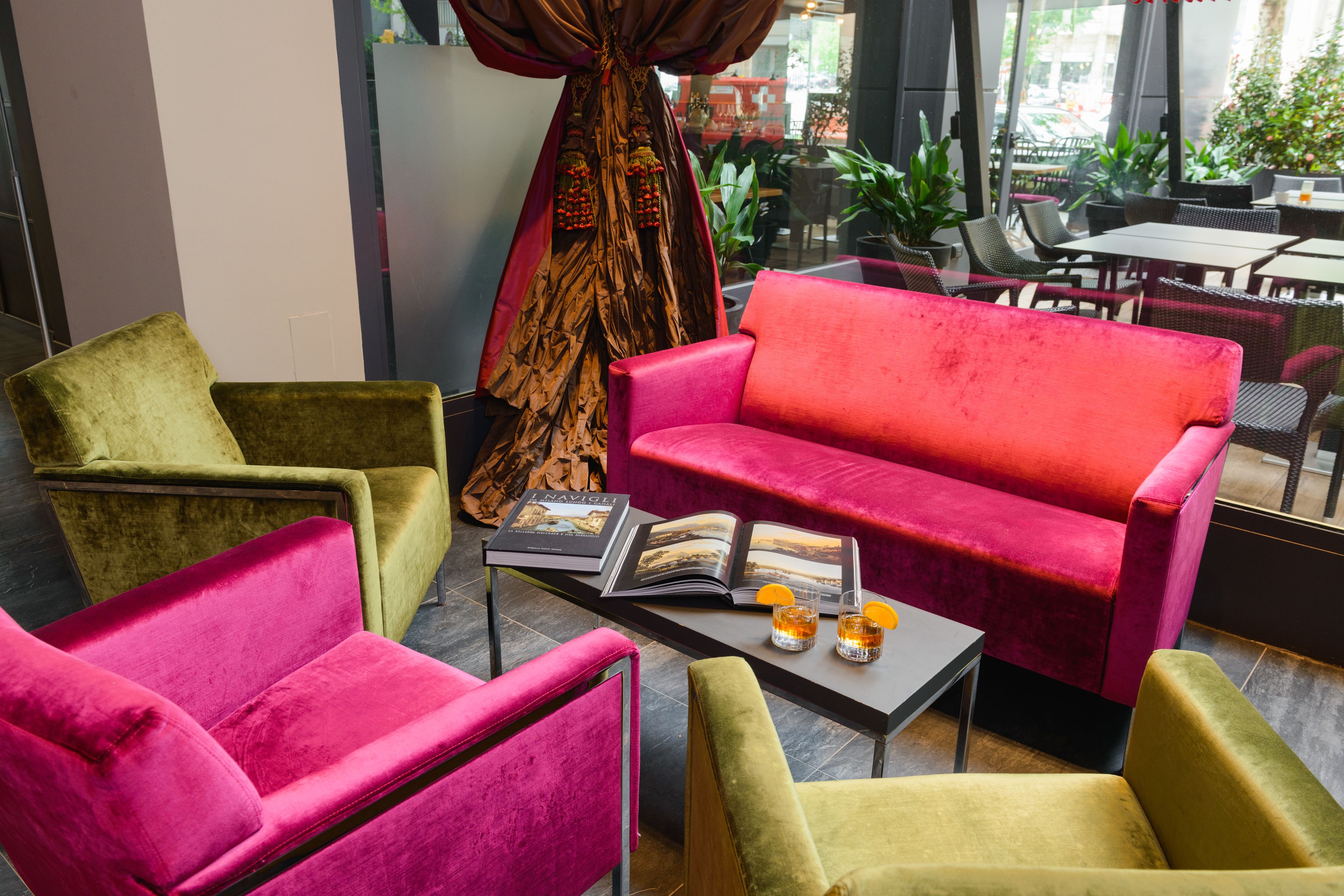 Een moderne zithoek met een rode bank, groene en roze fauteuils en een bijzettafeltje met een tijdschrift en drankjes.