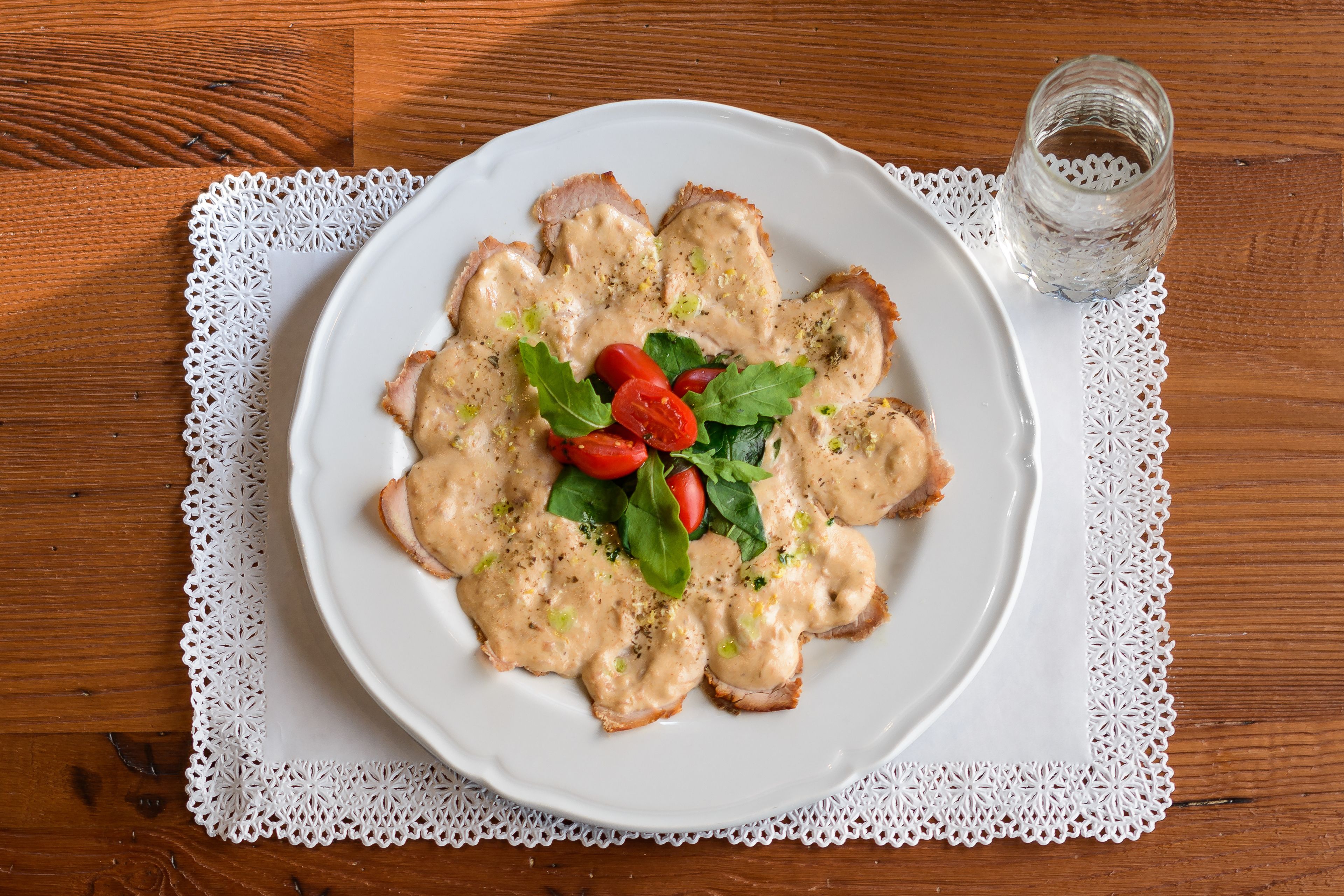 A plate of food with a white plate on a wooden table with a white lace doily.