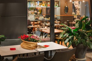 Interior de un restaurante con mobiliario de mimbre, una mesa con un sobre rojo y una planta en maceta.