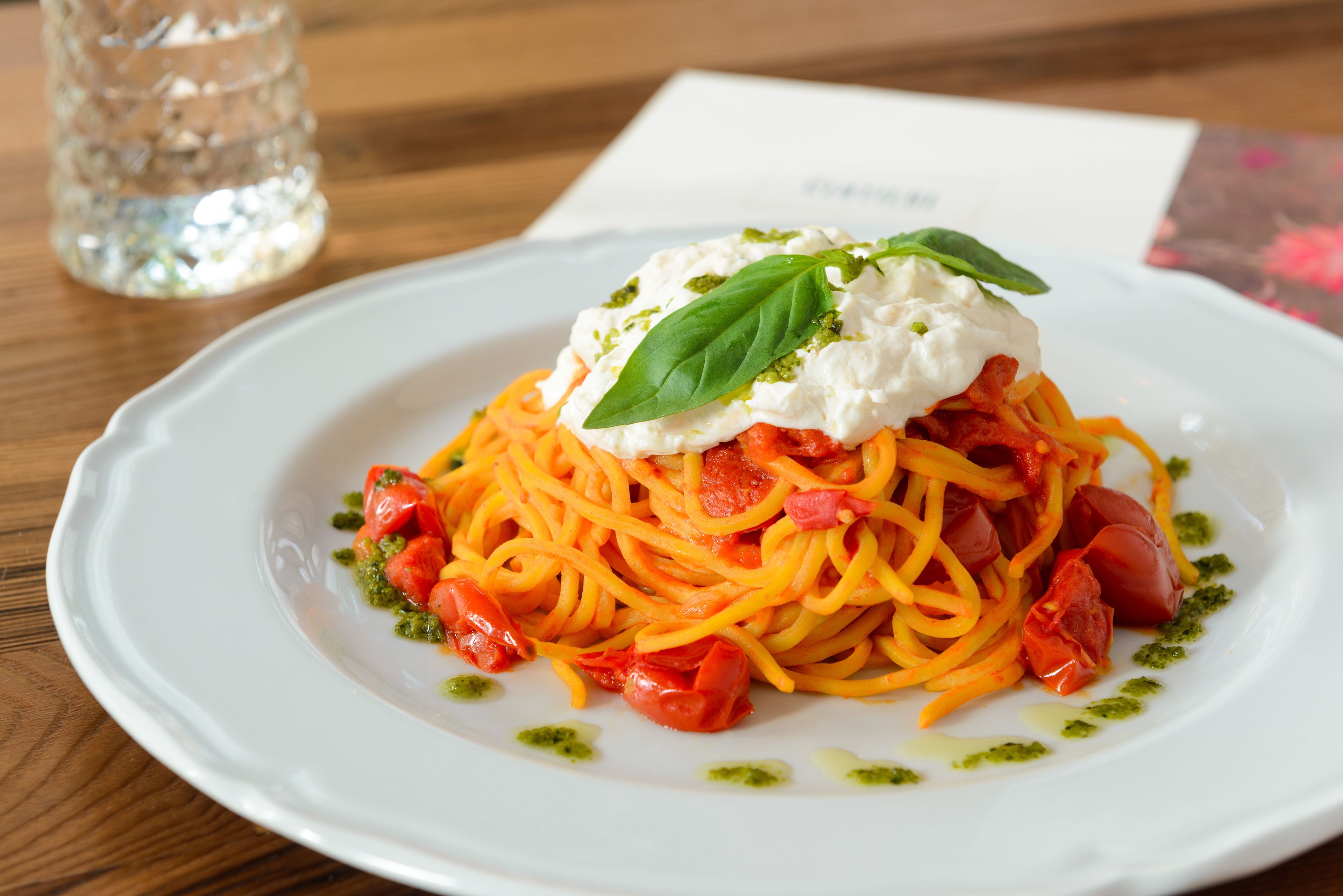 Ein Teller Spaghetti mit Tomatensauce, garniert mit einem Klecks Sahne und einem Basilikumblatt.