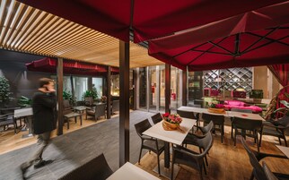 Una moderna sala da pranzo interna con mobili in vimini, ombrelloni rossi e un ingresso visibile a un'altra zona.