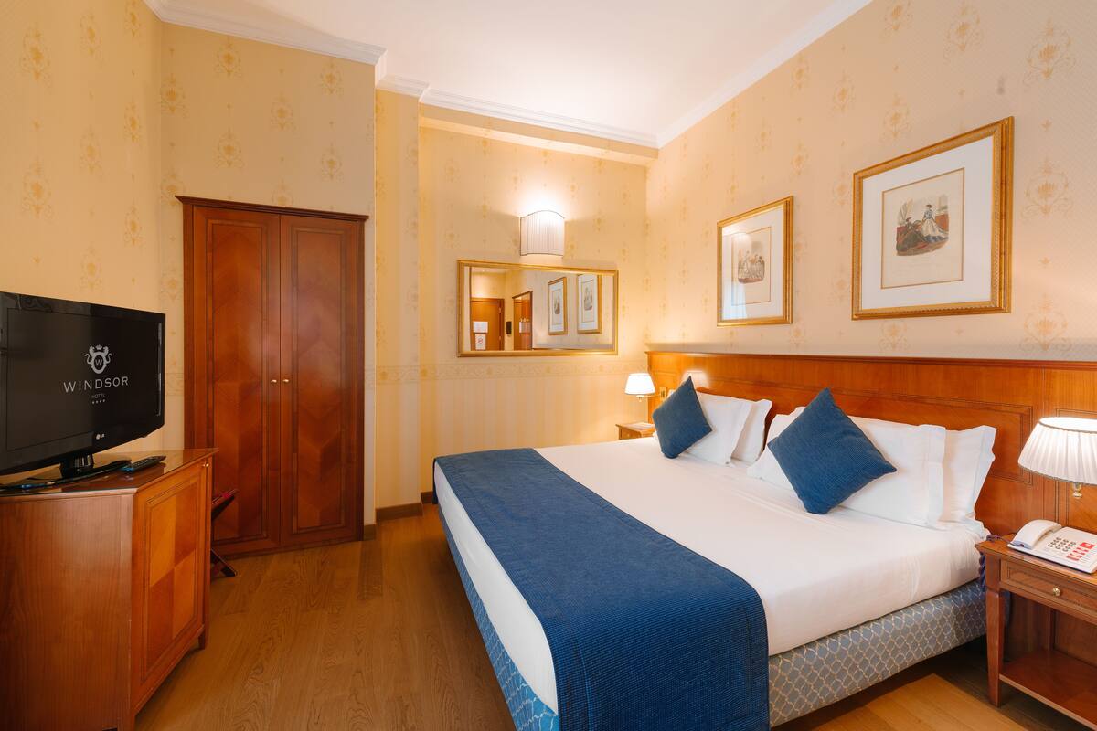 A hotel room with a large bed, a television, a wardrobe, and framed pictures on the wall.