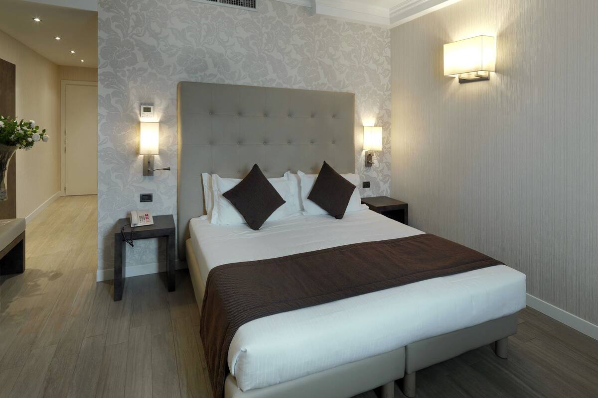 A hotel room with a large bed, two bedside tables, a wall-mounted light, and a telephone on one of the tables.