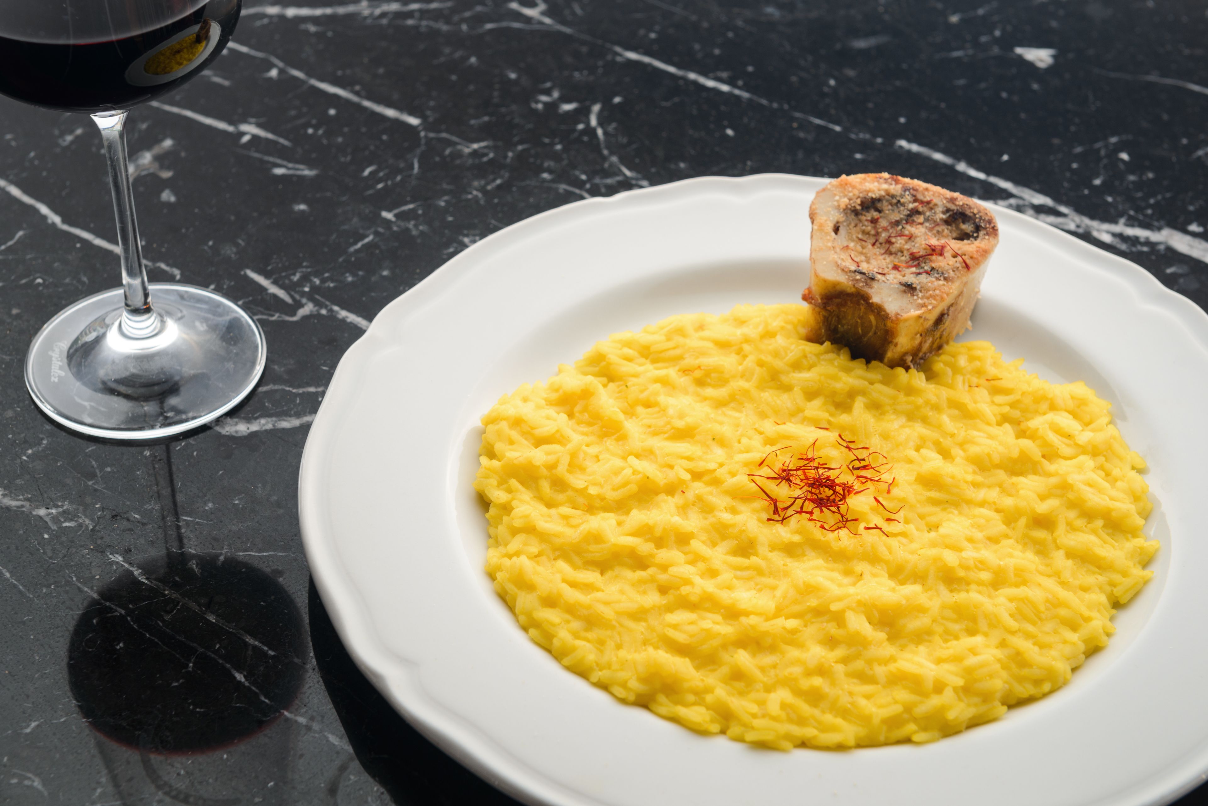 A plate of scrambled eggs with a slice of meat on top, accompanied by a glass of red wine on a marble surface.