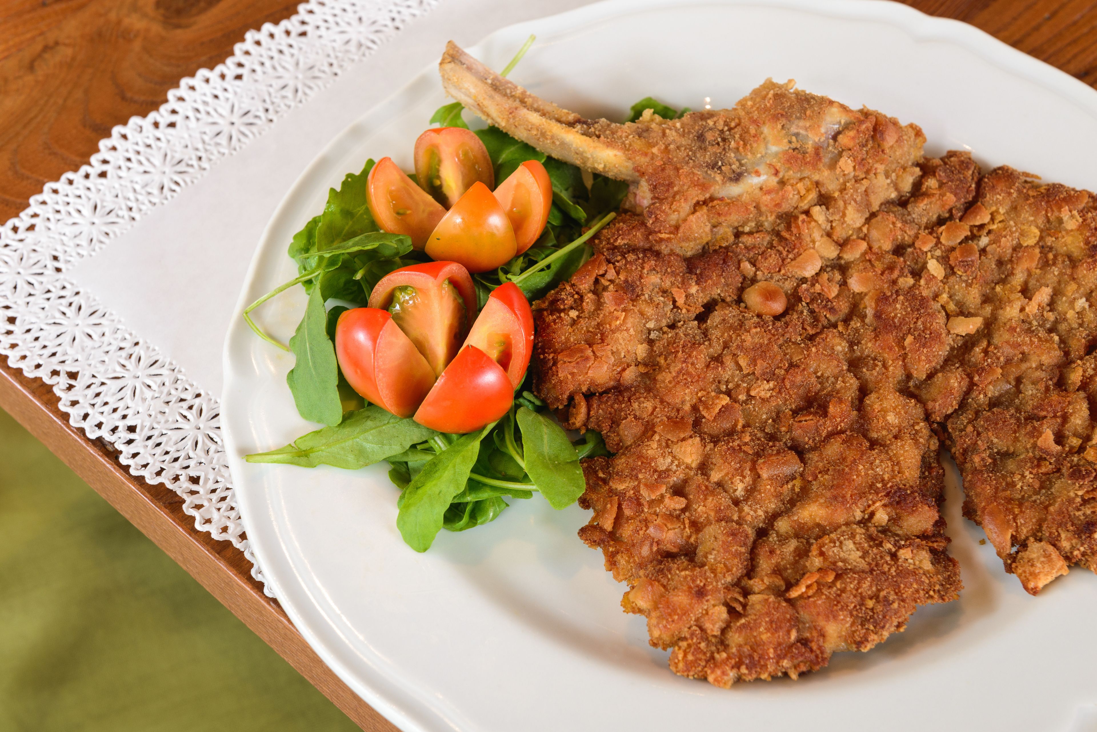 Un piatto con una costoletta impanata, pomodorini e verdure su un piatto bianco.