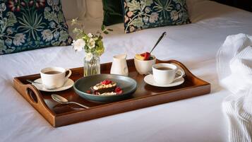 Ein Tablett mit Frühstücksangeboten, darunter Kaffee, eine Obstschale und ein Dessert, auf einem Bett mit Blumenkissen.