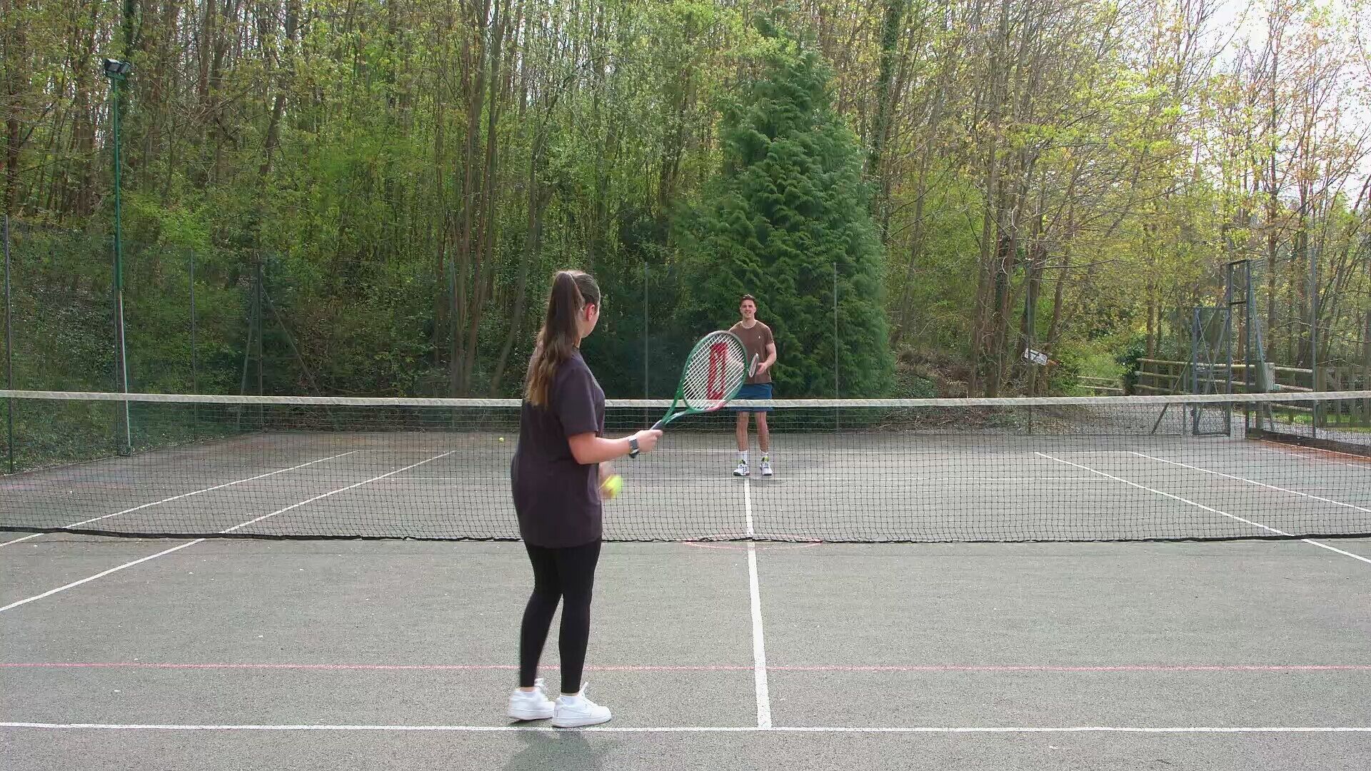 Una cancha de tenis con red, rodeada de árboles.