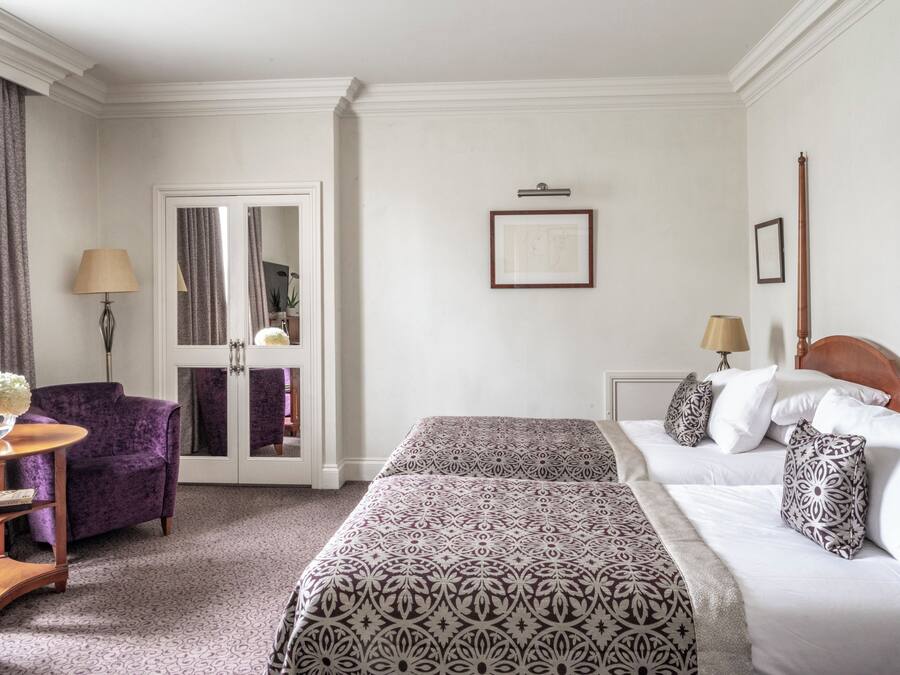 A hotel room with two beds, a sitting area with a purple chair, a small table, and a mirror.
