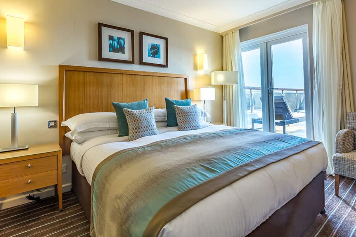 A hotel room with a large bed, a nightstand, a chair, and a balcony with a view.
