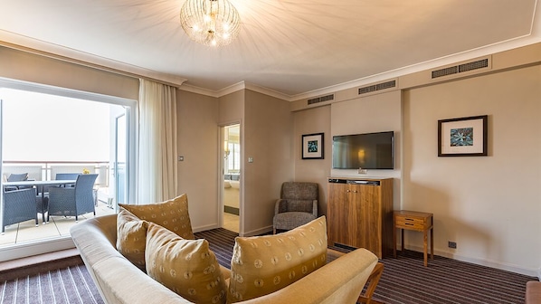 A modern hotel room with a sofa, armchair, TV, and a view to the outside.