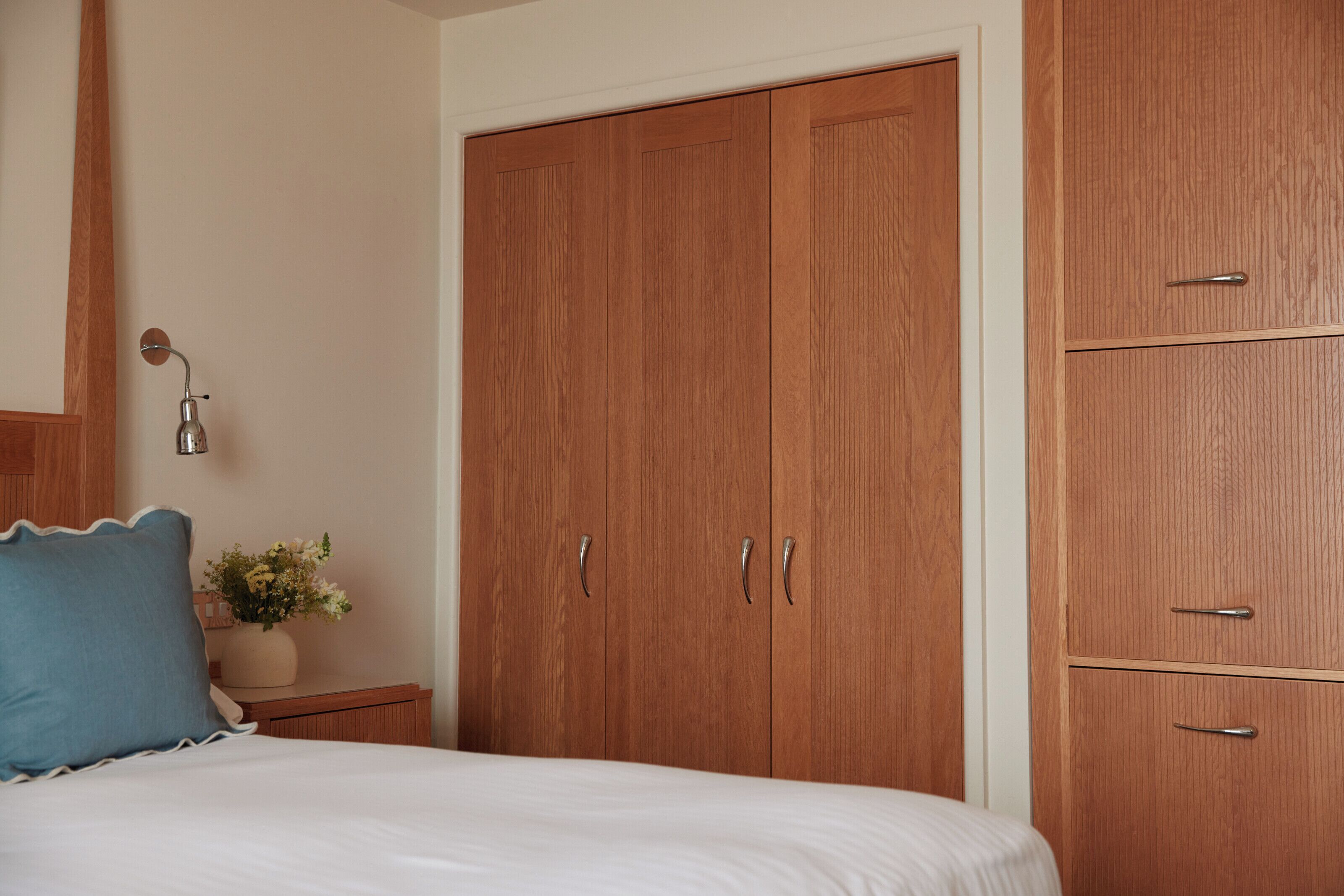 Un dormitorio con una cama, una mesita de noche, una lámpara, una planta en maceta y armarios de madera.