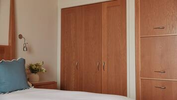 A bedroom with a bed, a nightstand, a lamp, a potted plant, and wooden wardrobes.