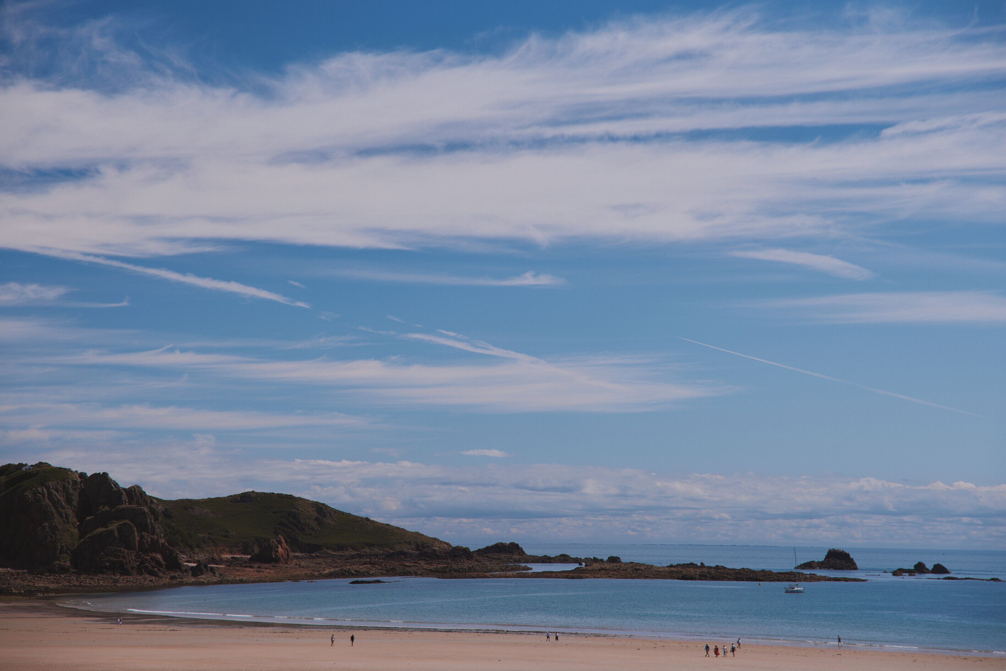 Una playa con cielos despejados, agua tranquila y afloramientos rocosos.