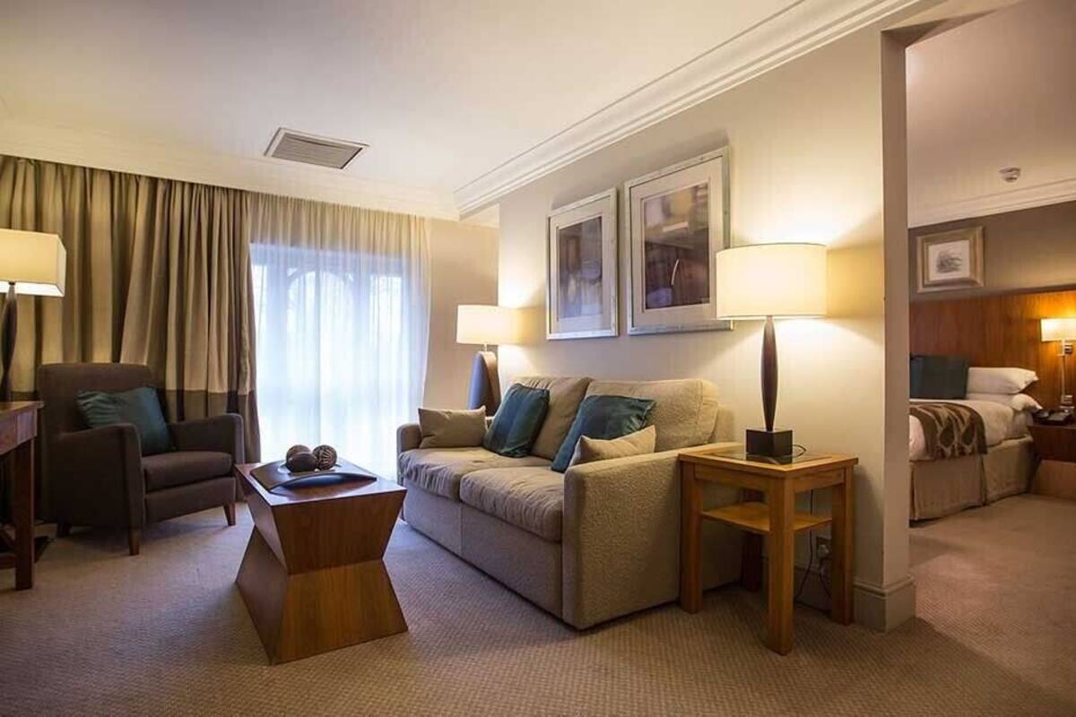 A hotel room with a sofa, armchair, and a small table. There are two lamps on the side tables.