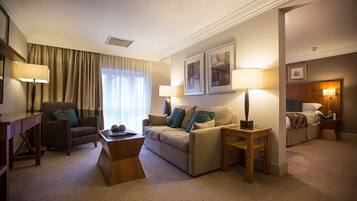 A hotel room with a sofa, armchair, and a small table. There are two lamps on the side tables.