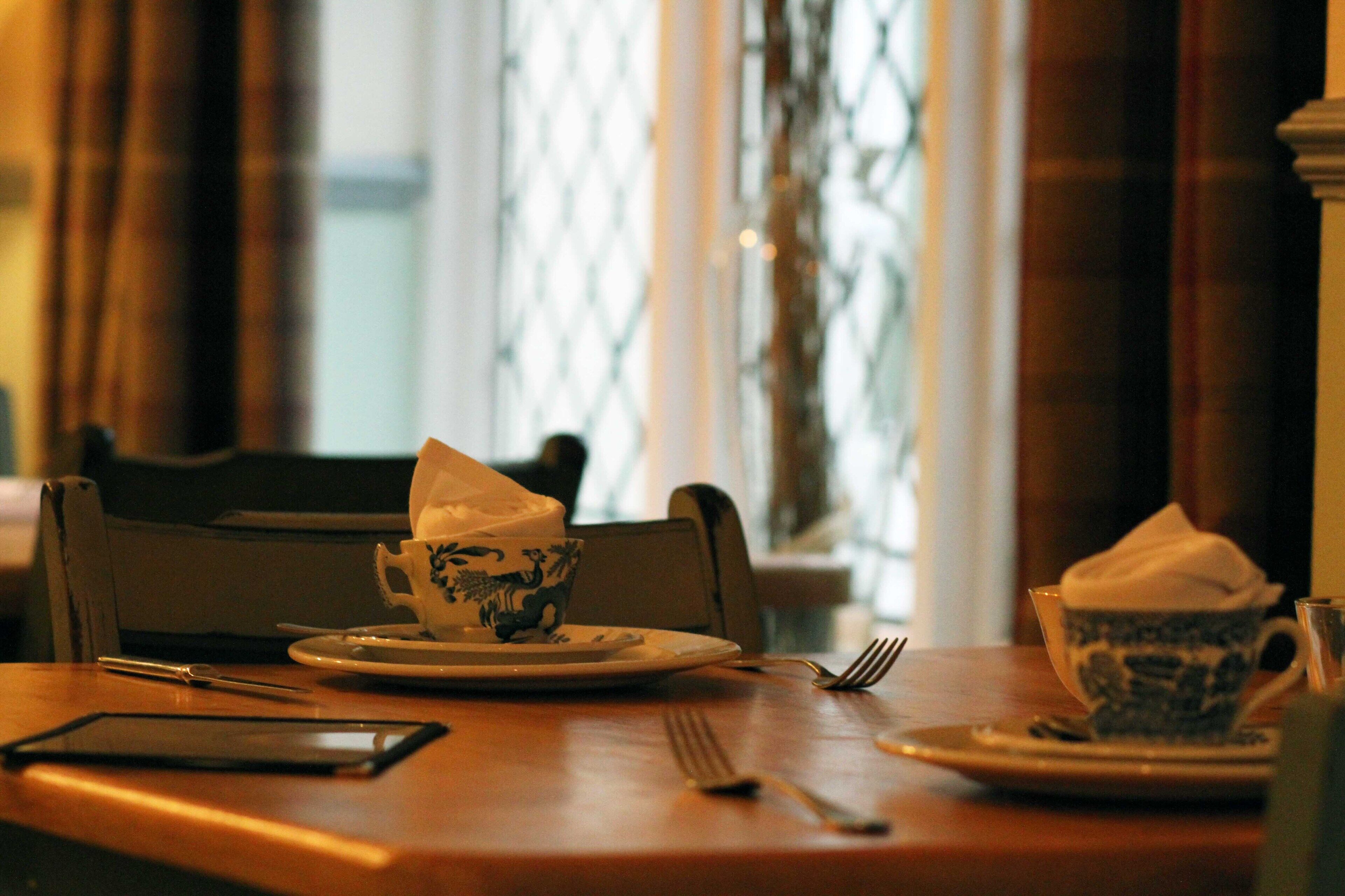 Una mesa de comedor con una taza y plato, un teléfono inteligente y un tenedor.