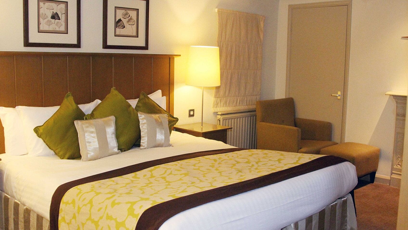 Une chambre d’hôtel avec un grand lit, une chaise, une lampe et deux tableaux encadrés au mur.