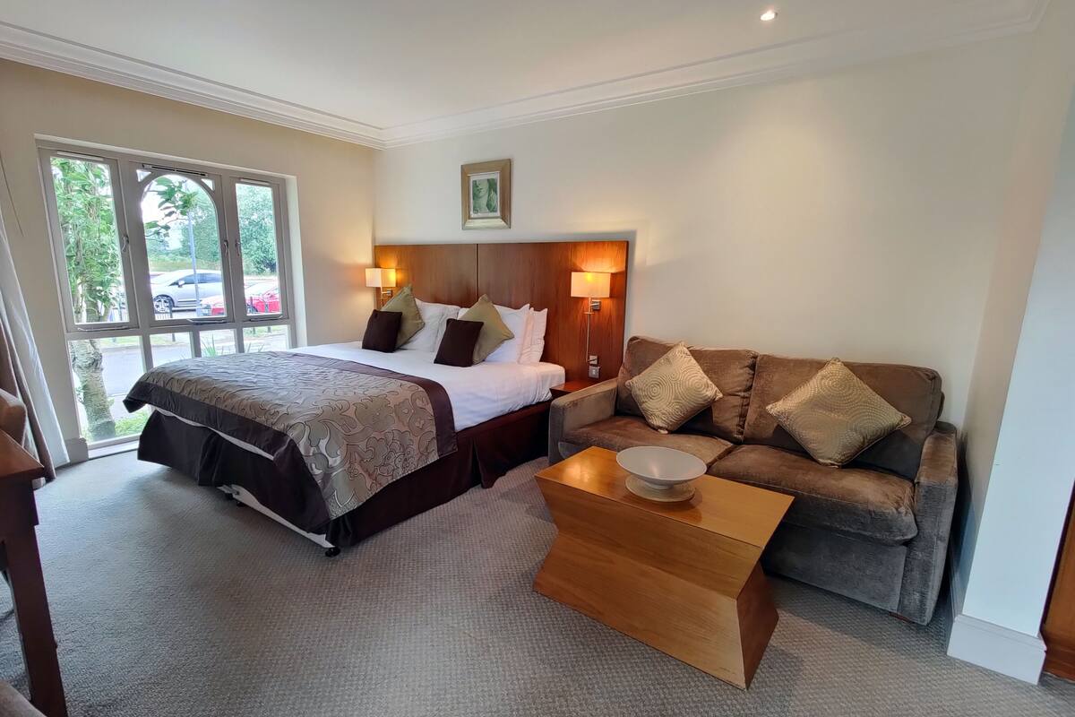A hotel room with a bed, a sofa, a coffee table, and a window with a view of the outside.