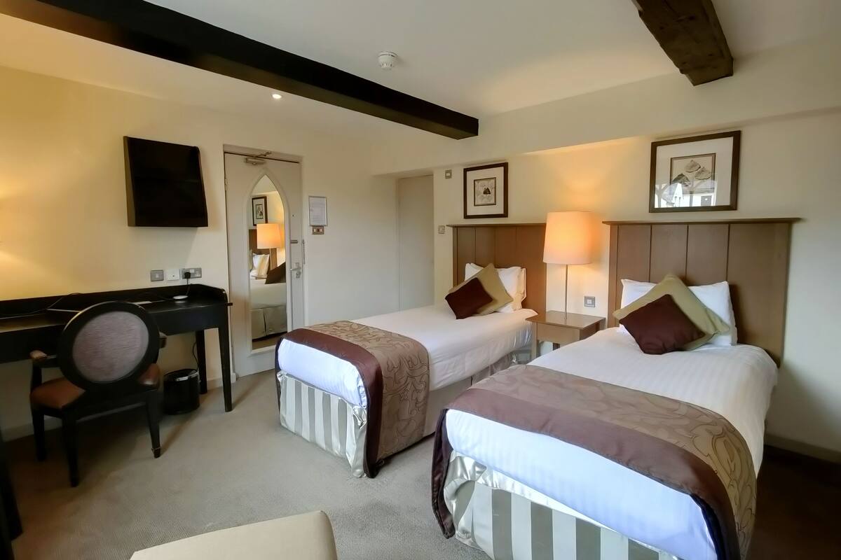 A hotel room with two beds, a desk, a chair, and a mirror.
