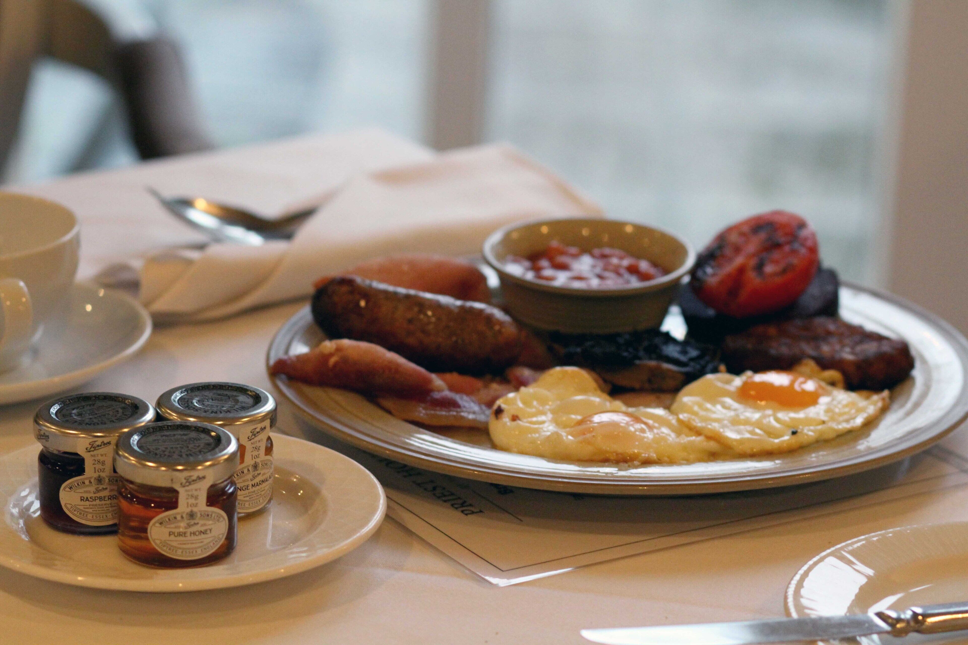 A breakfast plate with eggs, sausages, and jam.