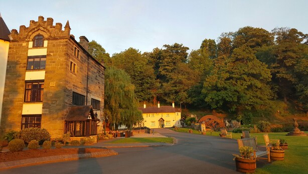 A historic stone building with a turret and a traditional yellow house with a garden in front. - The Priest House Hotel (Derby)