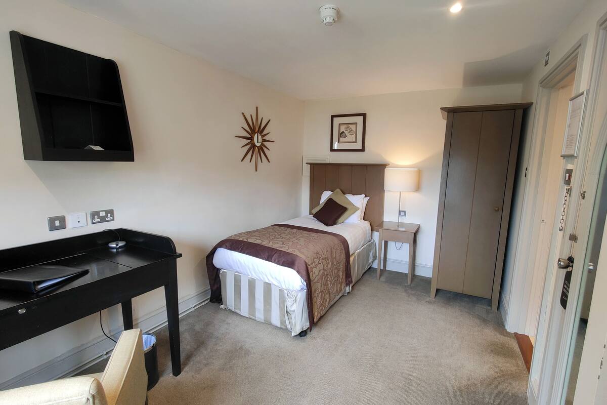 A hotel room with a bed, desk, chair, and a wardrobe.