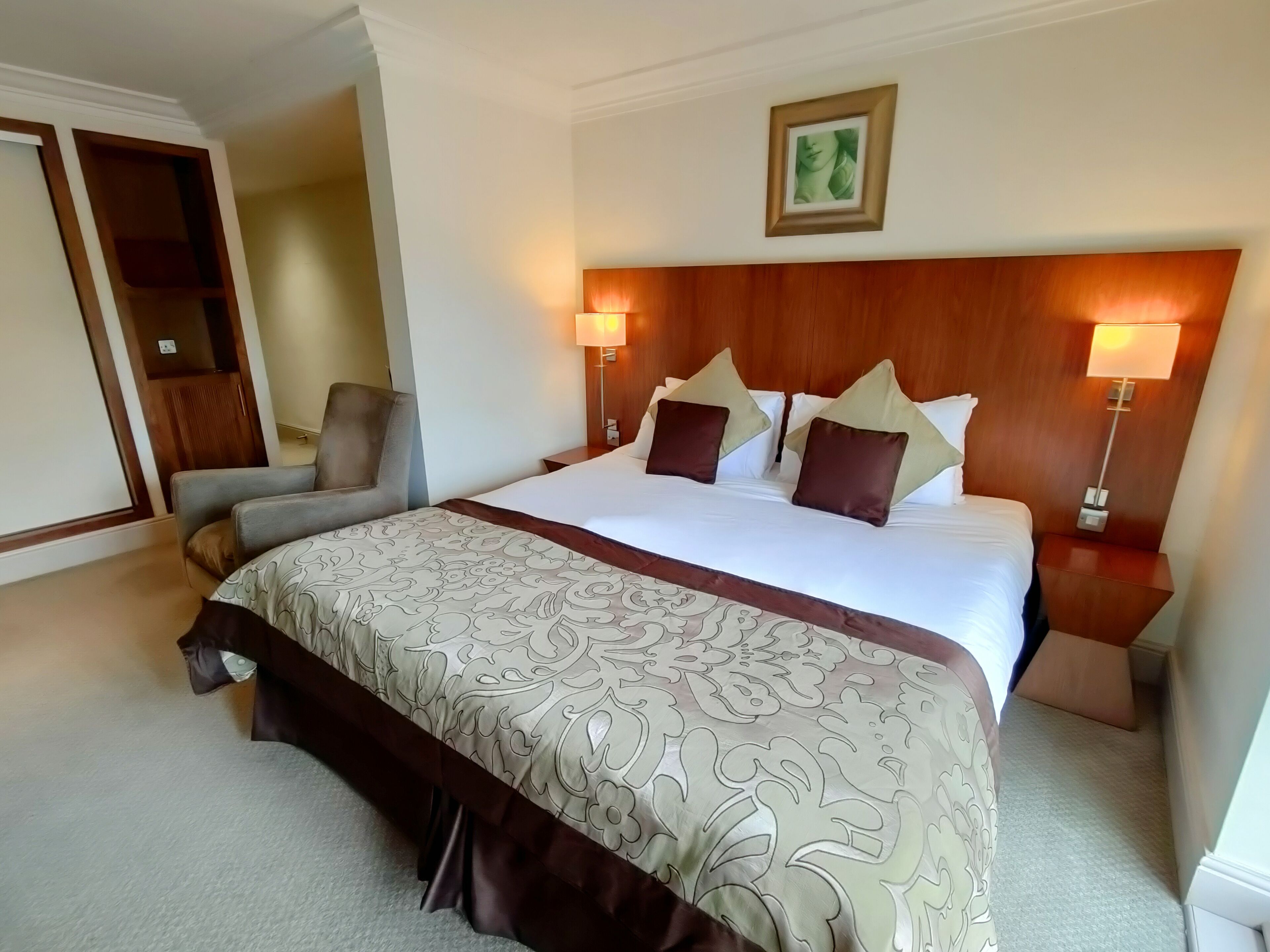 A hotel room with a large bed, two bedside tables, a chair, and a wooden headboard.