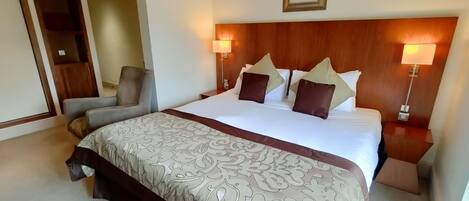 A hotel room with a large bed, two bedside tables, a chair, and a wooden headboard.