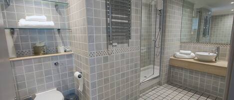 A modern bathroom with a glass-enclosed shower, a toilet, a trash bin, and a sink with a mirror above it.