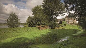 A rustic stone building with a traditional design, surrounded by lush greenery and a small stream.