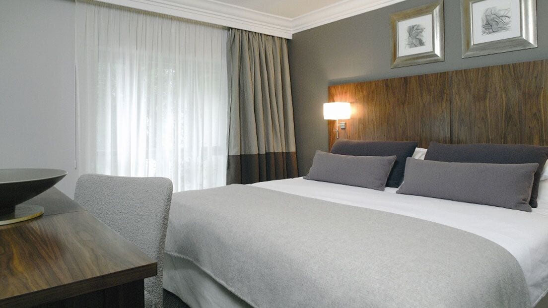 A hotel room with a large bed, a desk, and a lamp.