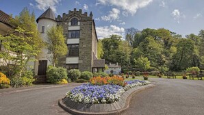 A historic stone building with a turret and a garden with flower beds. - The Priest House Hotel (Derby)