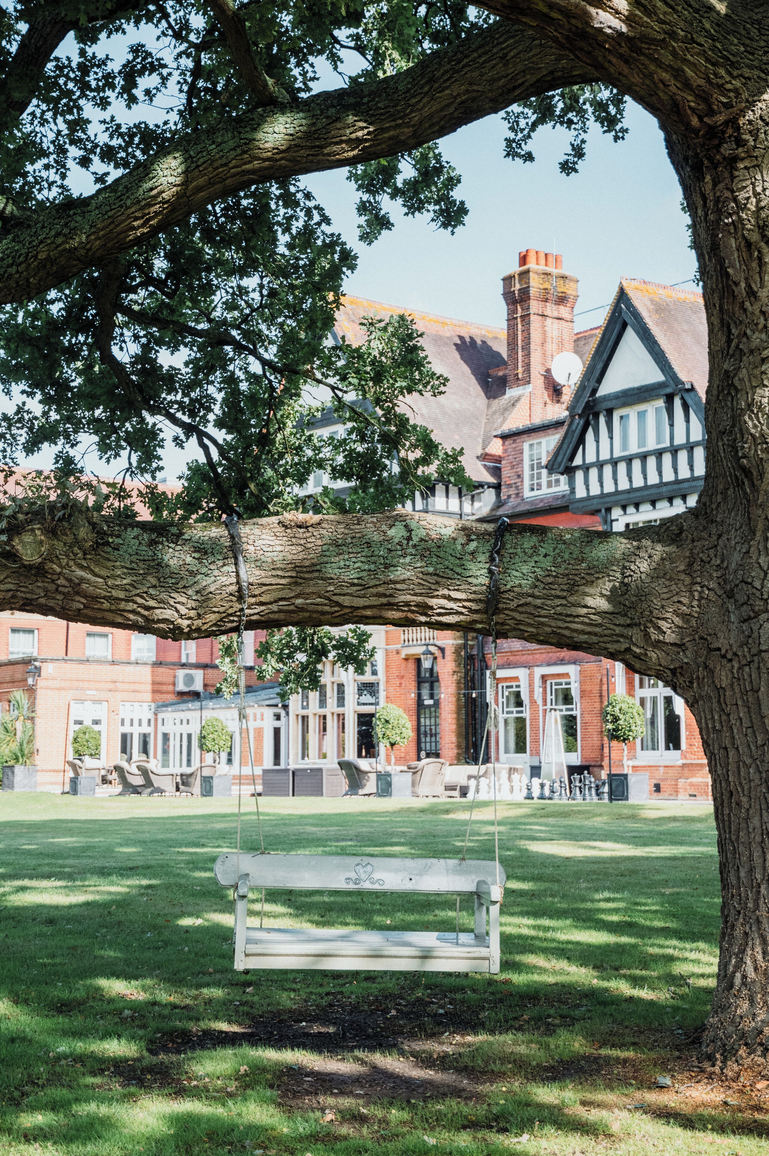A park with a bench, a tree, and a building with red brick walls and white trim.